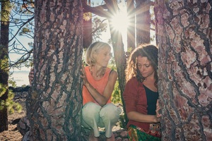 zwei Frauen sitzen auf einem großen Pinienbaum, die Sonne strahlt hinter ihnen